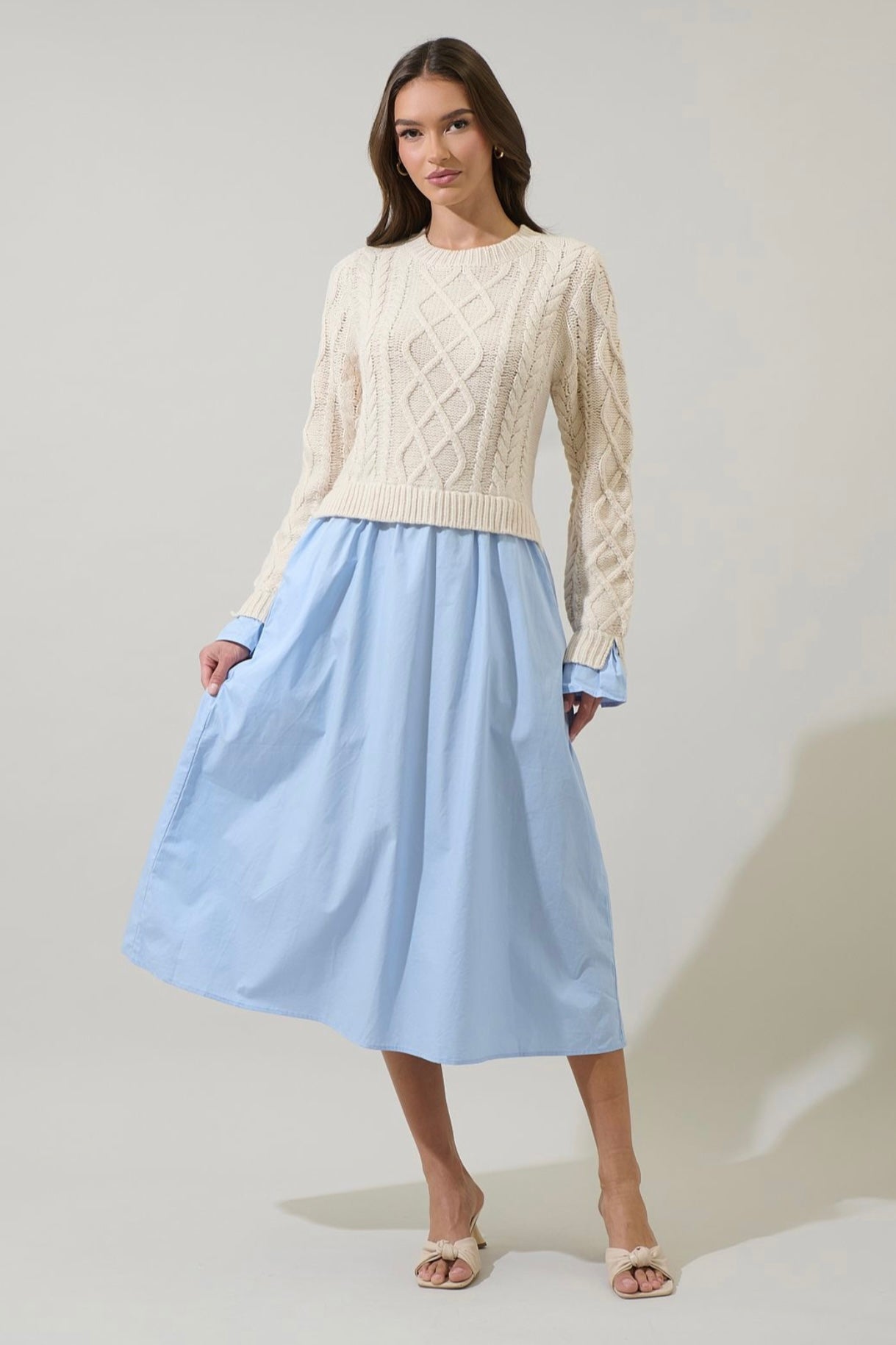 Woman wearing a cream cable-knit sweater and a blue midi skirt, perfect for casual and chic occasions.