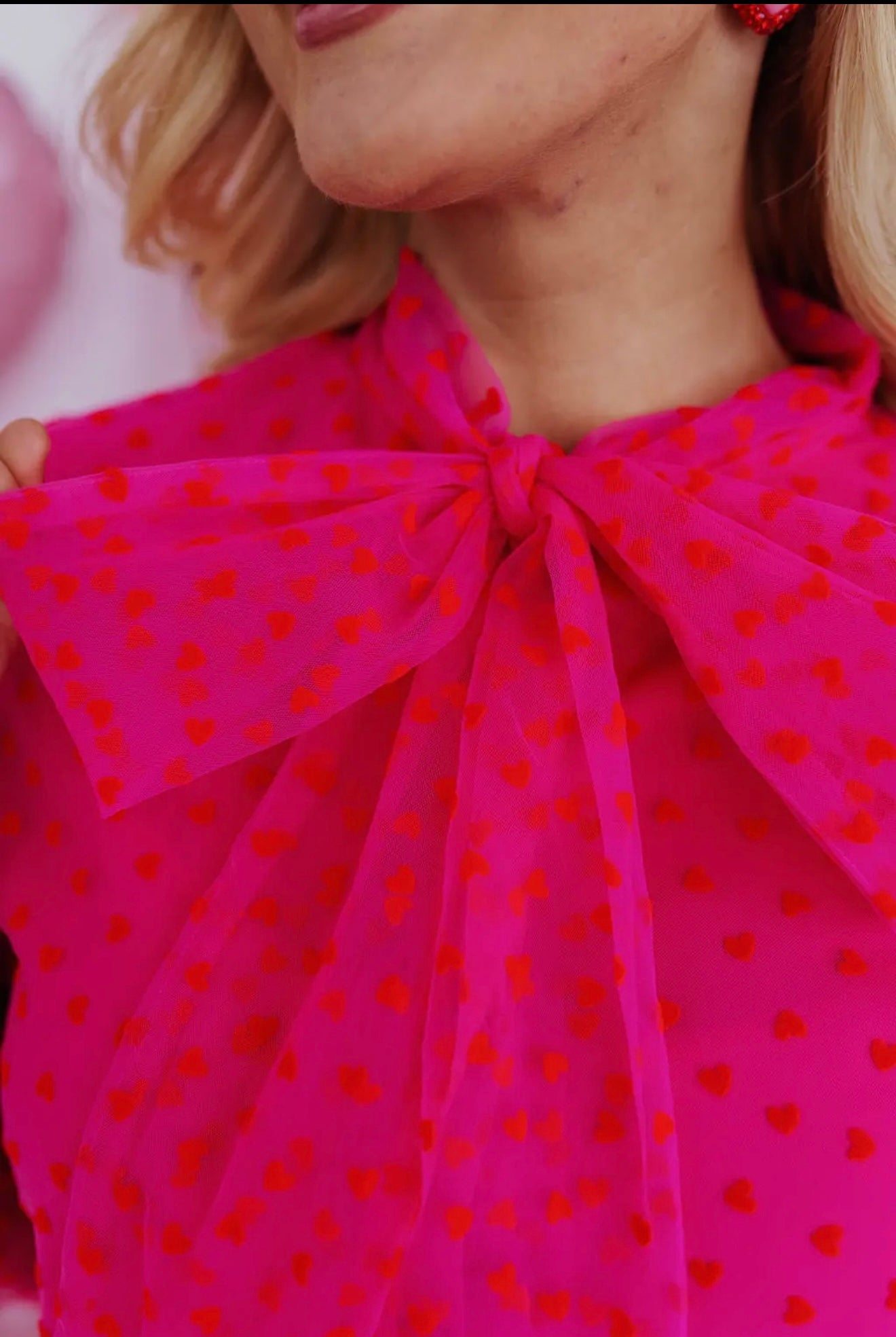 Bright pink sheer blouse with red heart details and a stylish bow tie at the neckline.