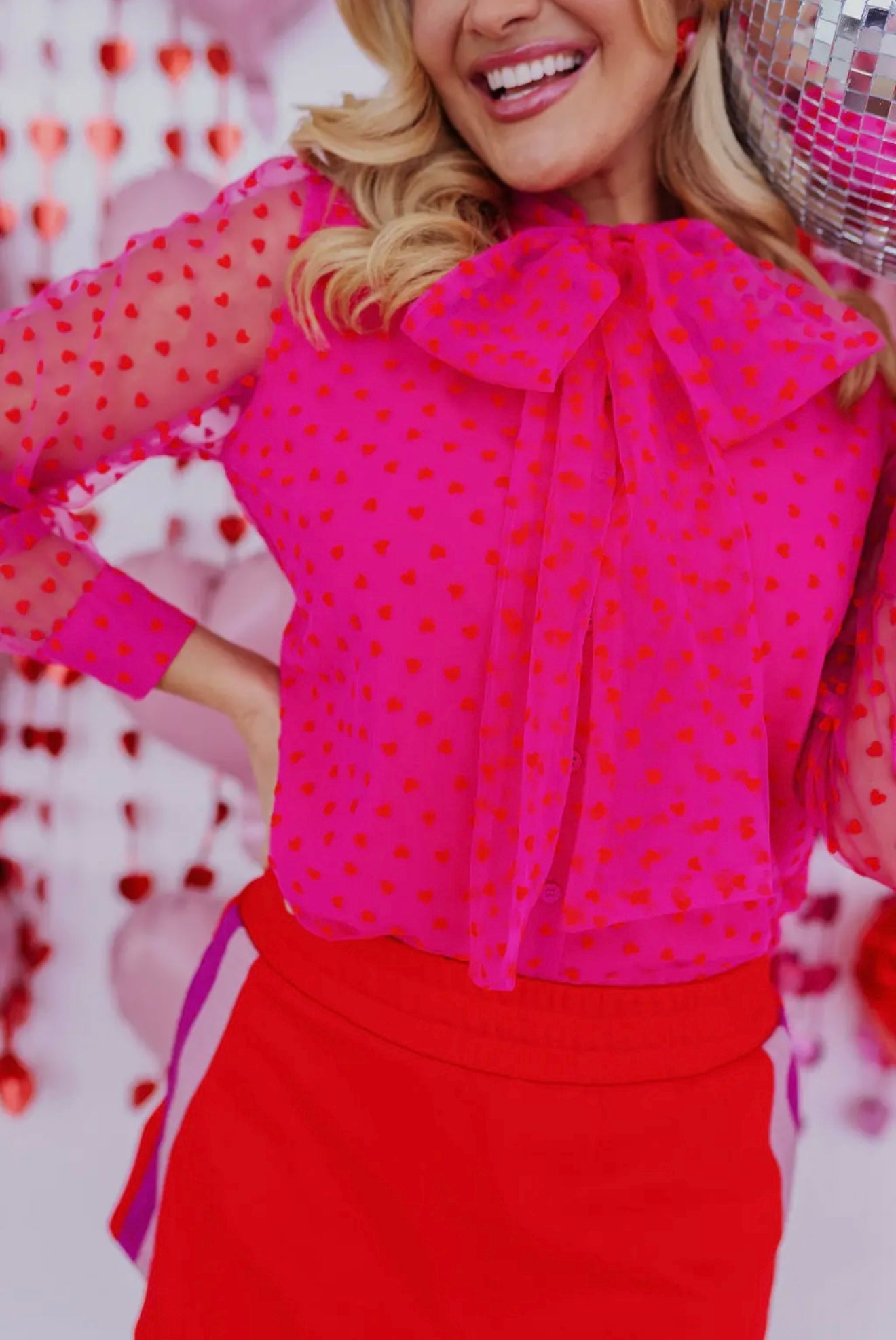 Bright pink blouse with red heart patterns and bow neckline, paired with a red skirt, perfect for festive occasions.